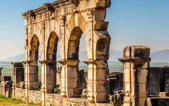 Ancient Roman arches at Volubilis near Fes, Morocco, with distant hills.