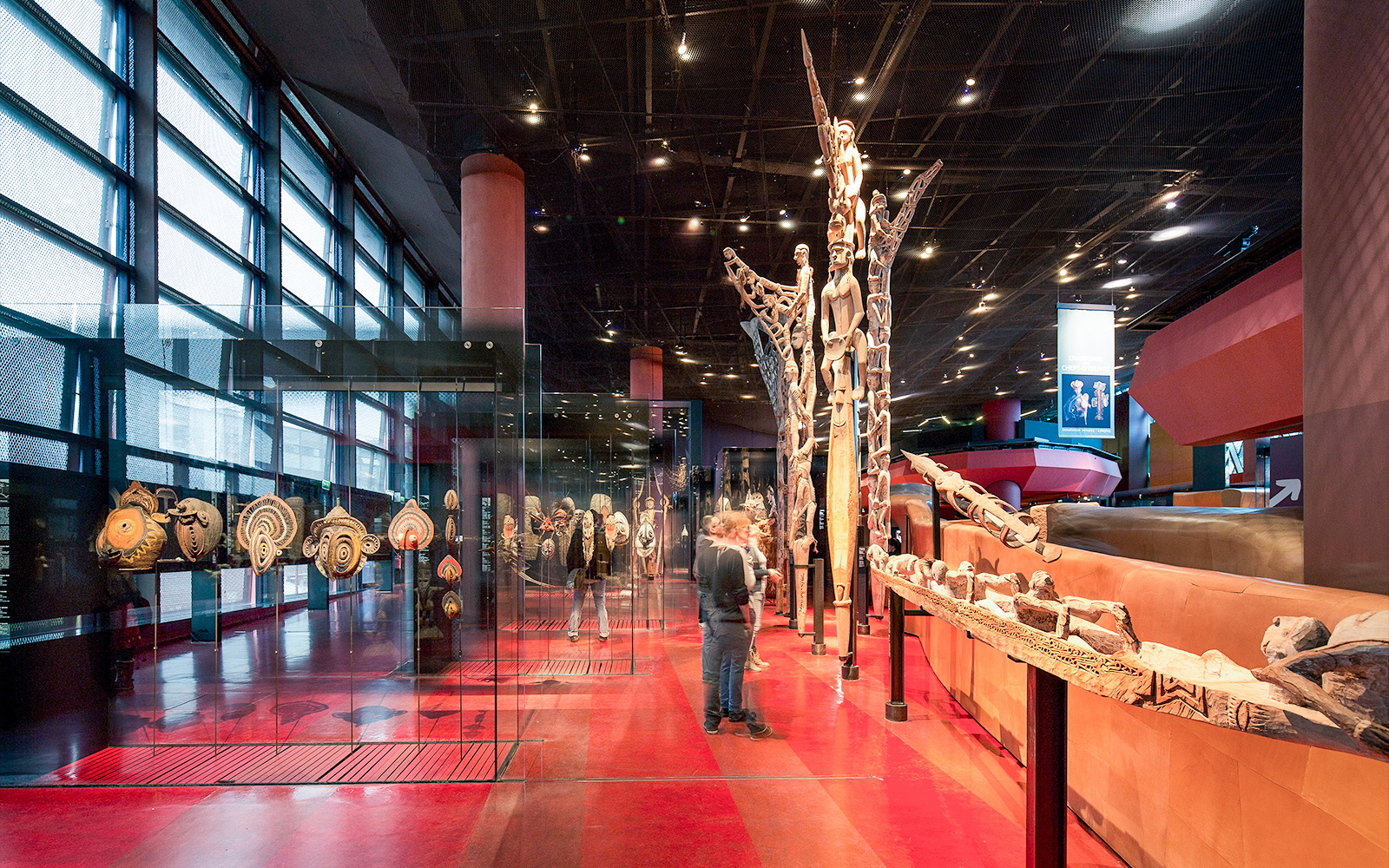 Musee du Quai Branly interior with tribal art displays and visitors exploring exhibits.