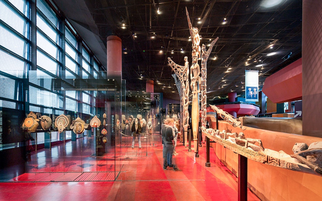 Musee du Quai Branly interior with tribal art displays and visitors exploring exhibits.