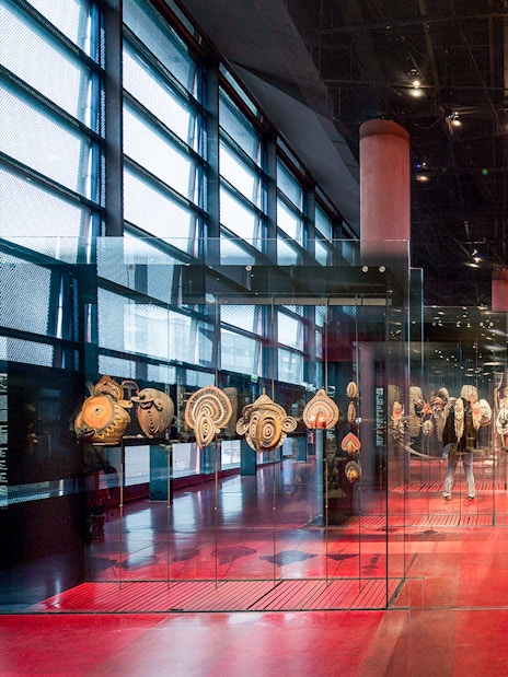 Musee du Quai Branly interior with tribal art displays and visitors exploring exhibits.