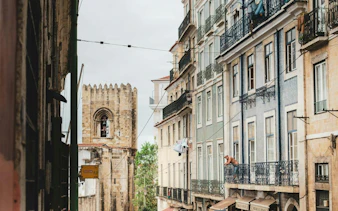 Narrow street view in Lisbon with historic buildings and a glimpse of the Lisbon Cathedral.