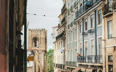 Narrow street view in Lisbon with historic buildings and a glimpse of the Lisbon Cathedral.
