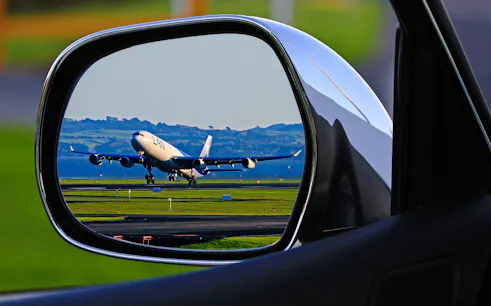 Airplane taking off viewed through car side mirror, representing Zanzibar airport transfers.