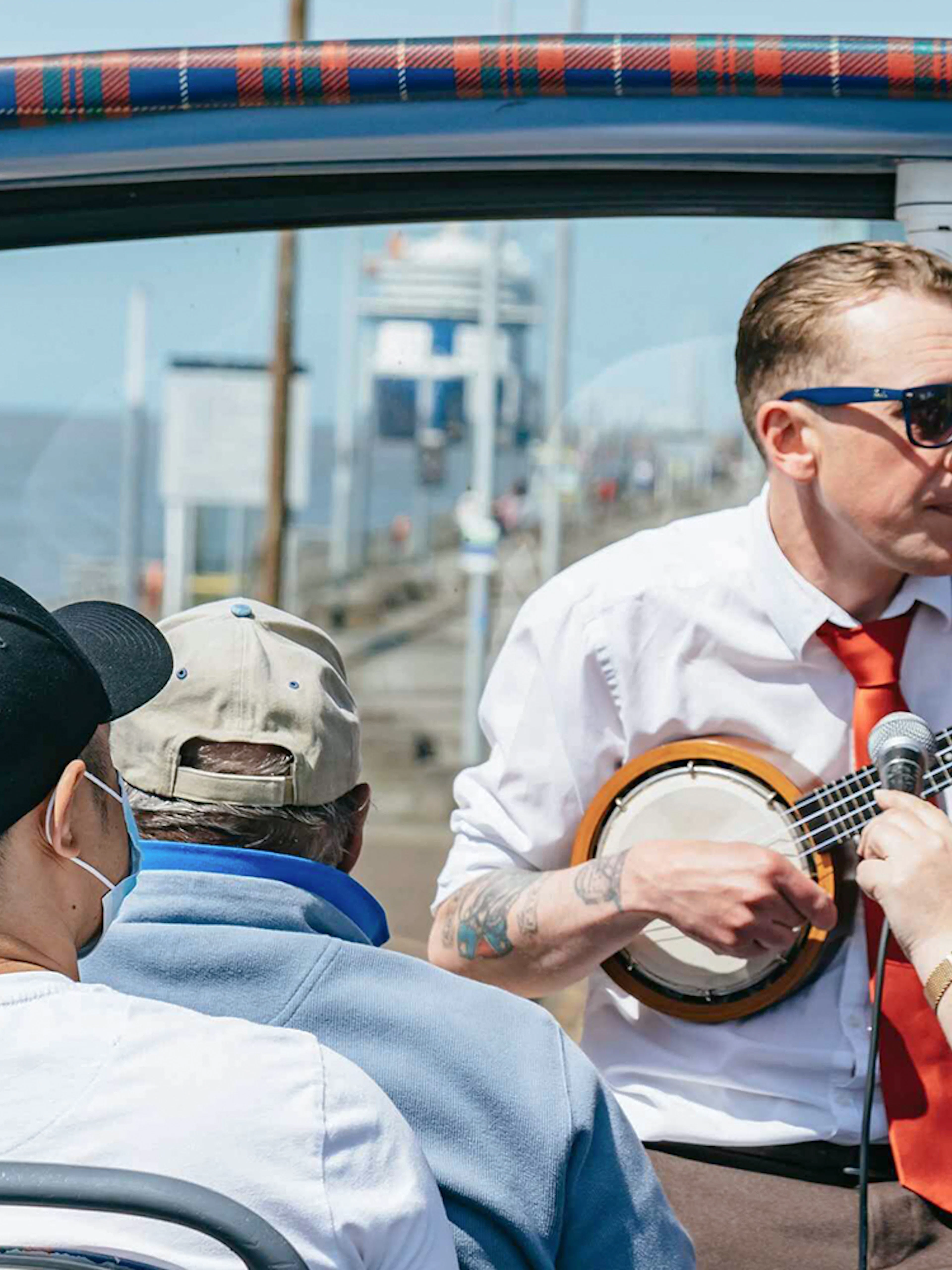 Guide playing banjo on Liverpool hop-on hop-off city and Beatles tour.