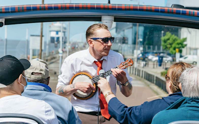Guide playing banjo on Liverpool hop-on hop-off city and Beatles tour.