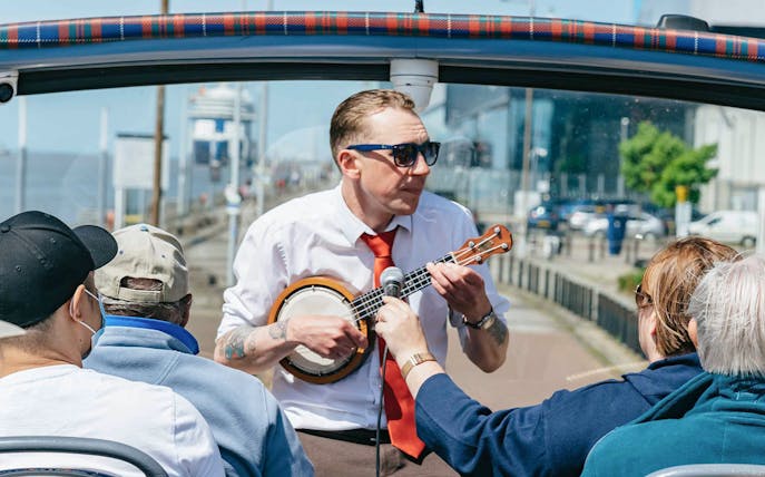 Guide playing banjo on Liverpool hop-on hop-off city and Beatles tour.