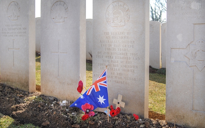 Australian soldier's grave with flag and poppies at Somme battlefield cemetery.