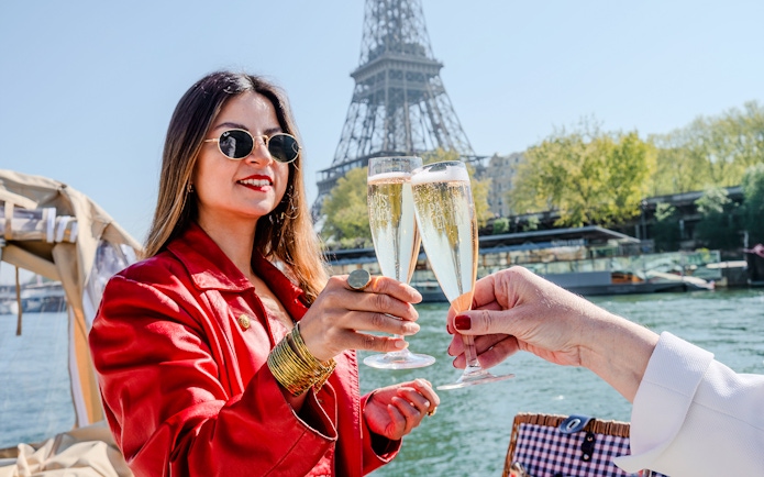 Clinking champagne glasses on Seine cruise with Eiffel Tower in background.