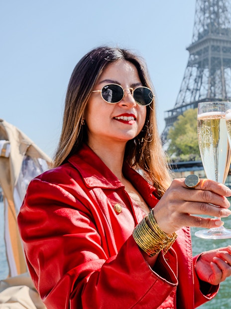 Clinking champagne glasses on Seine cruise with Eiffel Tower in background.
