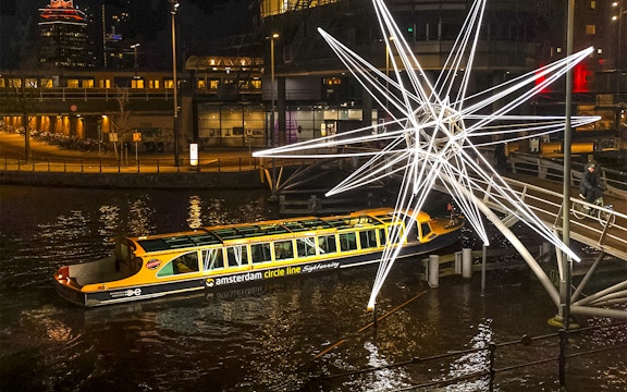 Amsterdam canal cruise passing illuminated star sculpture during Light Festival.