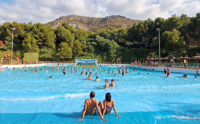 Visitors enjoying the wave pool at Aqualandia Benidorm, Spain, with scenic hills in the background.