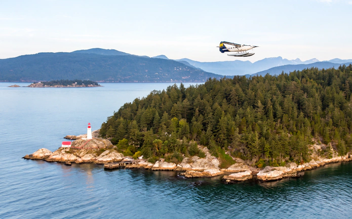 Seaplane flying over a forested island with a lighthouse in Vancouver.
