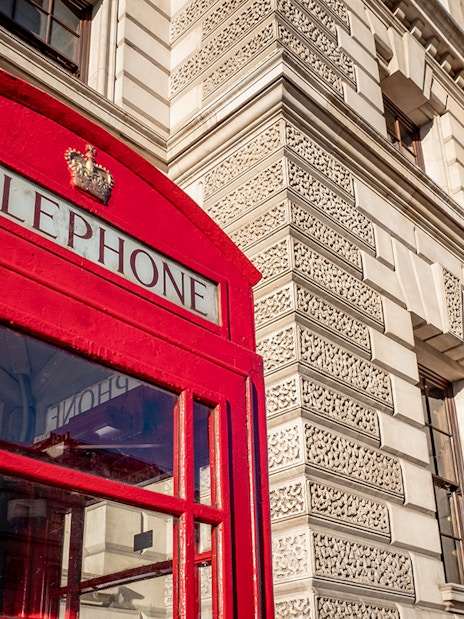 Red telephone box near historic building, London, featured in Harry Potter film locations tour.