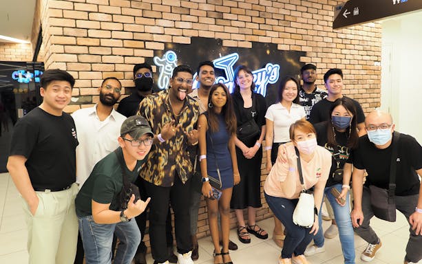 Group of people enjoying the Singapore FunVee Party Bus Pub Crawl in front of a neon sign.
