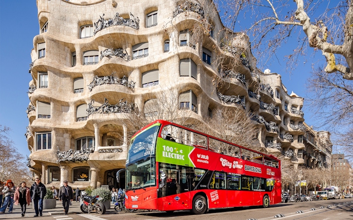 Barcelona hop-on hop-off bus in front of Casa Milà, a Gaudí architectural landmark.