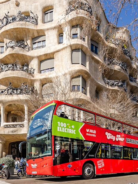 Barcelona hop-on hop-off bus in front of Casa Milà, a Gaudí architectural landmark.