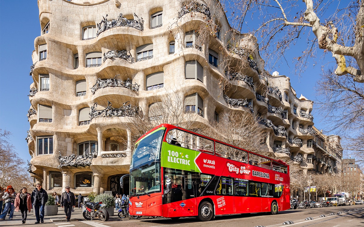 Barcelona hop-on hop-off bus in front of Casa Milà, a Gaudí architectural landmark.