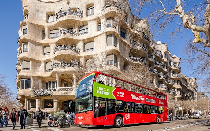 Barcelona hop-on hop-off bus in front of Casa Milà, a Gaudí architectural landmark.