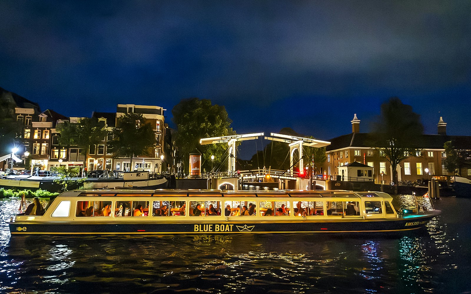 Evening canal cruise boat passing under illuminated bridge in Amsterdam.
