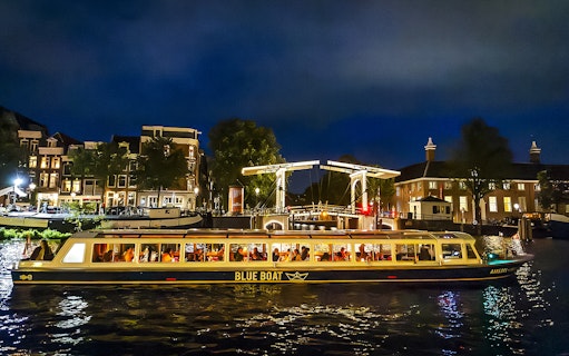 Evening canal cruise boat passing under illuminated bridge in Amsterdam.