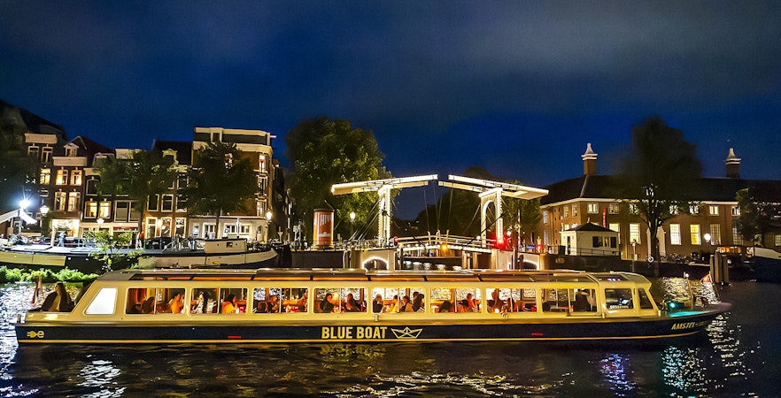 Evening canal cruise boat passing under illuminated bridge in Amsterdam.