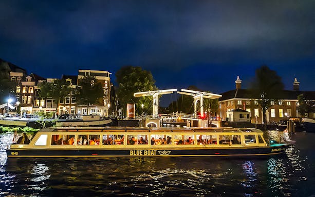 Evening canal cruise boat passing under illuminated bridge in Amsterdam.
