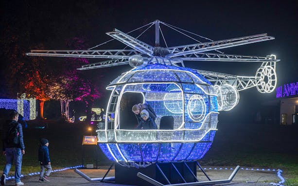 Illuminated helicopter installation at Lumina Park Wonderworld with visitors exploring inside.