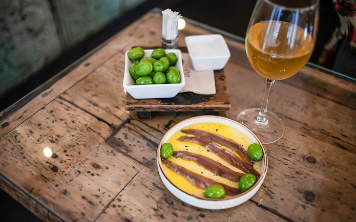 Anchovies and olives on a plate with a glass of wine, La Barceloneta food tour.