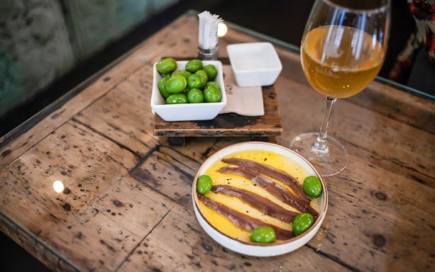 Anchovies and olives on a plate with a glass of wine, La Barceloneta food tour.