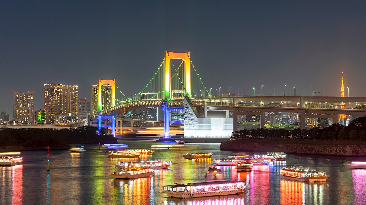 Cruise ships in Tokyo Bay at night with Rainbow Bridge illuminated in the background.