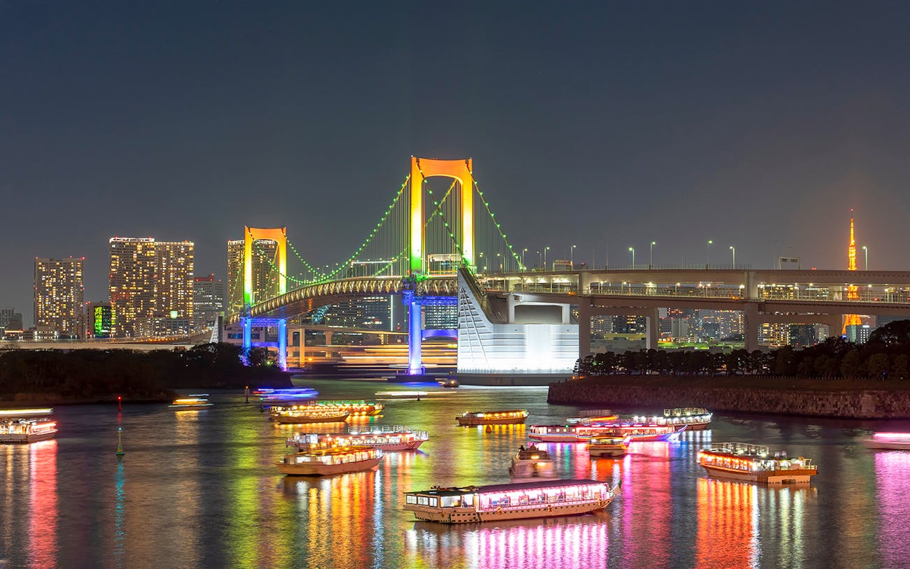 Cruise ships in Tokyo Bay at night with Rainbow Bridge illuminated in the background.