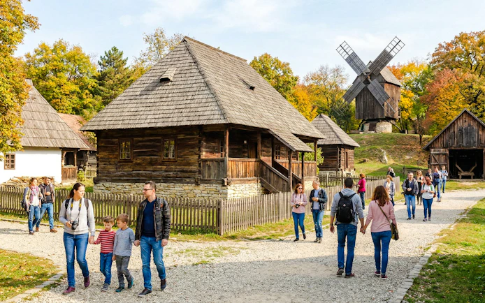 Visitors exploring traditional wooden houses and windmill at open-air Village Museum.