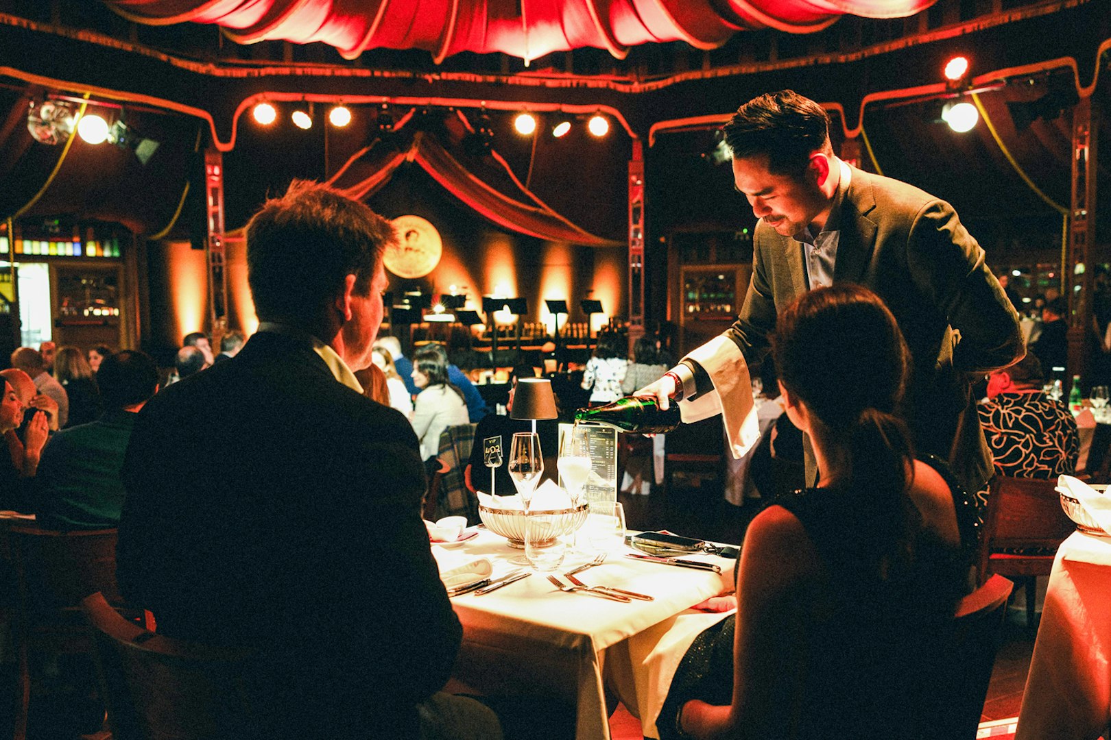 Server pouring wine at a candlelit dinner during a Strauss concert in Prater, Vienna.