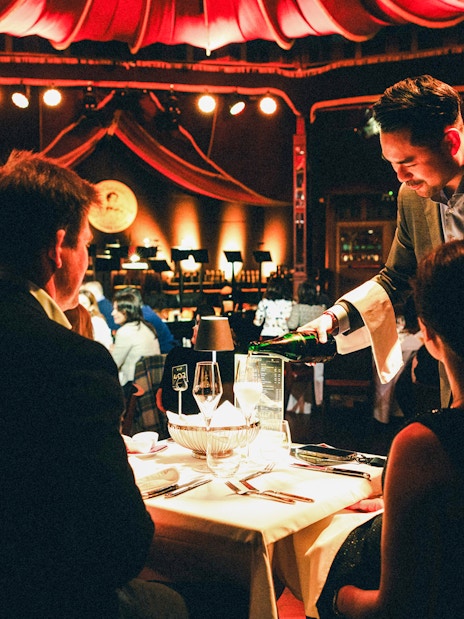 Server pouring wine at a candlelit dinner during a Strauss concert in Prater, Vienna.