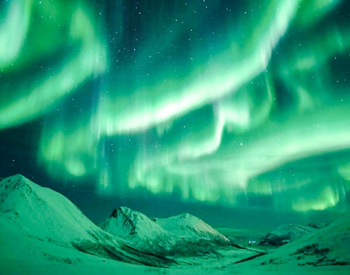 Northern Lights illuminating snowy mountains near Tromso, Norway.