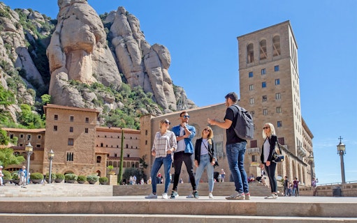 Tour group at Montserrat Monastery with guide, rocky mountain backdrop, Spain.