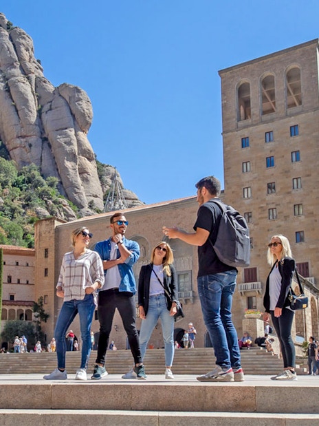 Tour group at Montserrat Monastery with guide, rocky mountain backdrop, Spain.