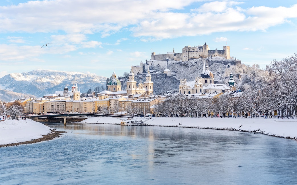 Salzburg castle overlooking snowy cityscape and river in winter.