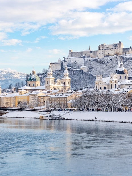 Salzburg castle overlooking snowy cityscape and river in winter.