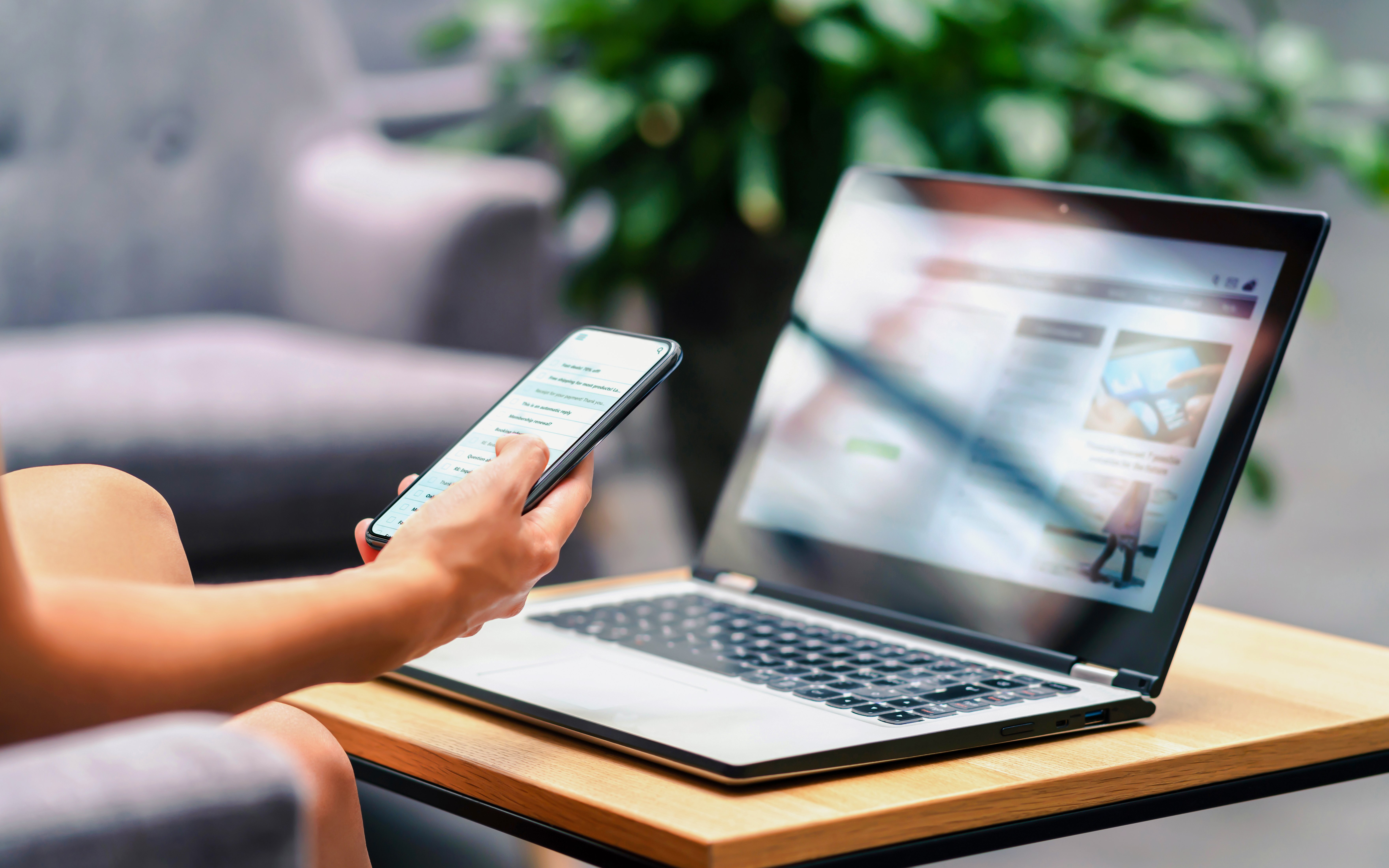 Person using smartphone and laptop in a lounge with wifi access.