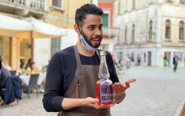 Man presenting a bottle of red aperitif on a street in Venice during the Ultimate Spritz Tour.
