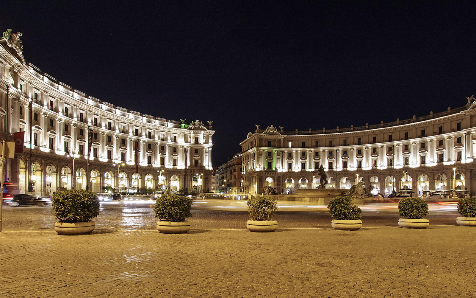 Republic Square in Rome, Italy, illuminated at night with historic buildings and a central fountain.