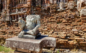 Headless stone statue on pedestal against brick walls at My Son Sanctuary, Vietnam.