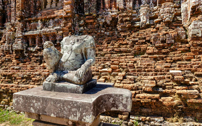 Headless stone statue on pedestal against brick walls at My Son Sanctuary, Vietnam.