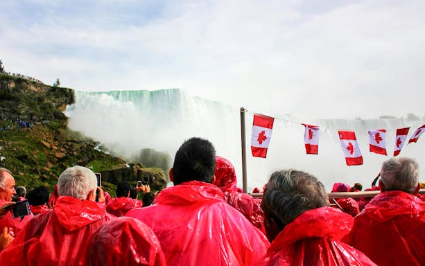 Tourists in red ponchos on a Niagara Falls cruise with Canadian flags.