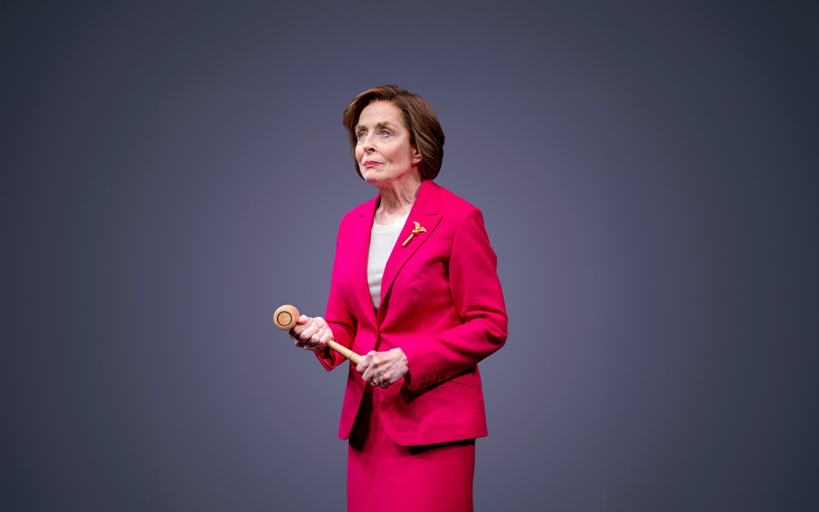 A person in a pink suit holding a gavel on stage.