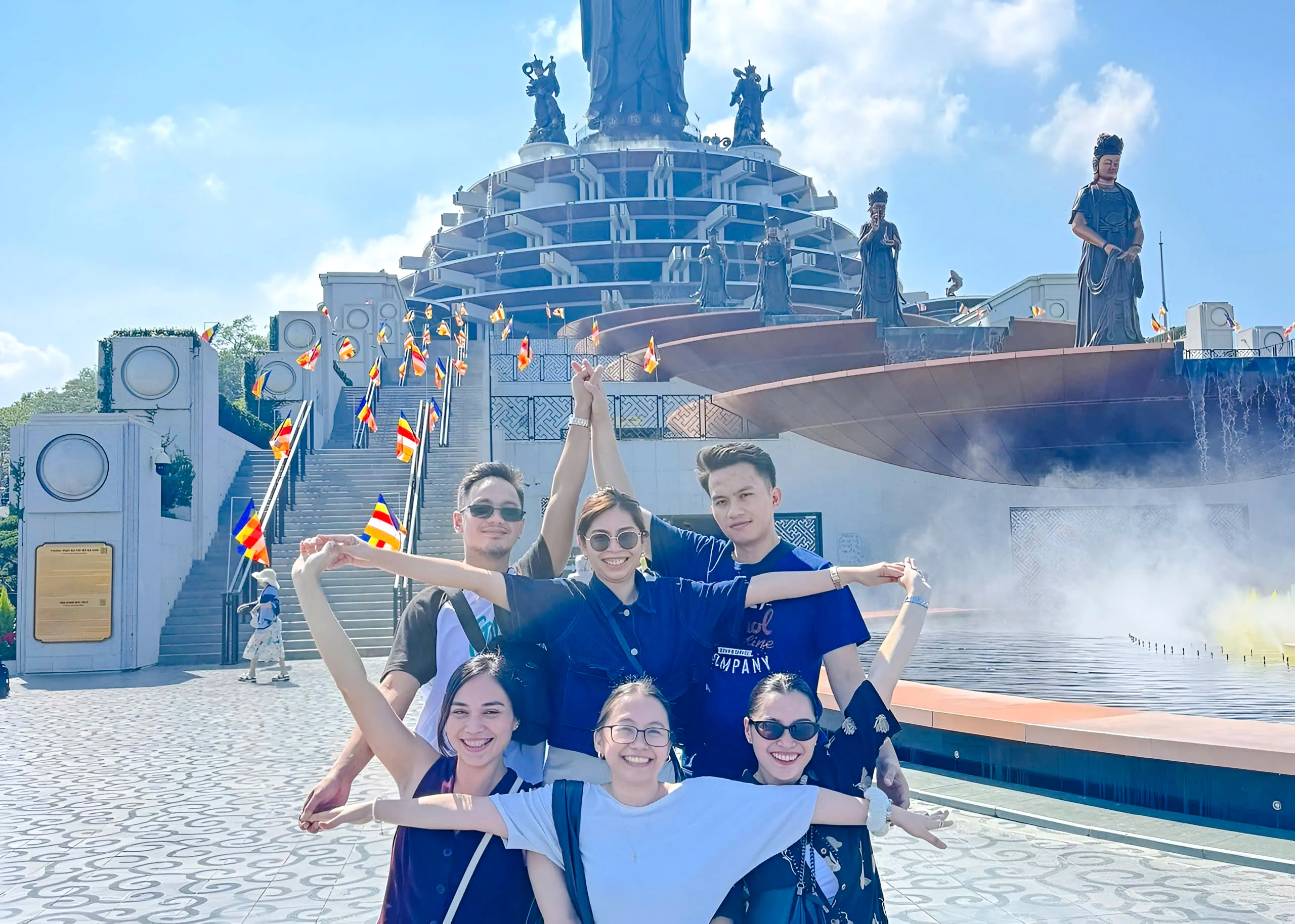 Group posing in front of Cao Dai Holy See, Tay Ninh, with statues and flags visible.