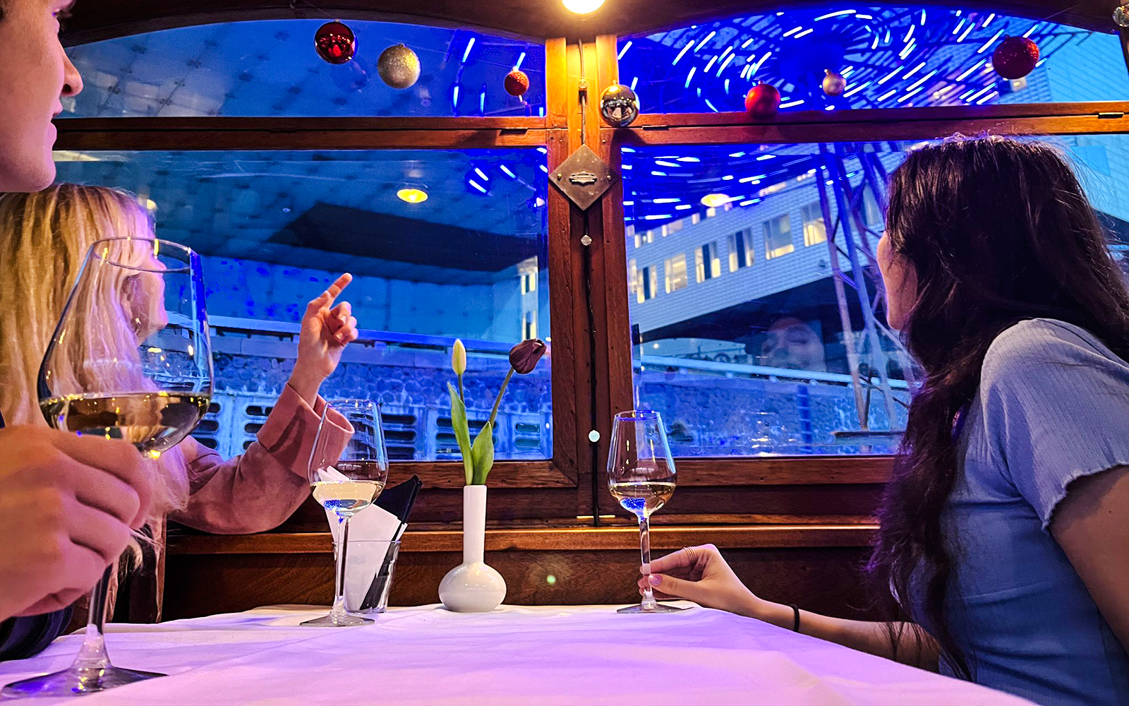 Guests enjoying wine on Amsterdam Light Festival cruise with cityscape view.
