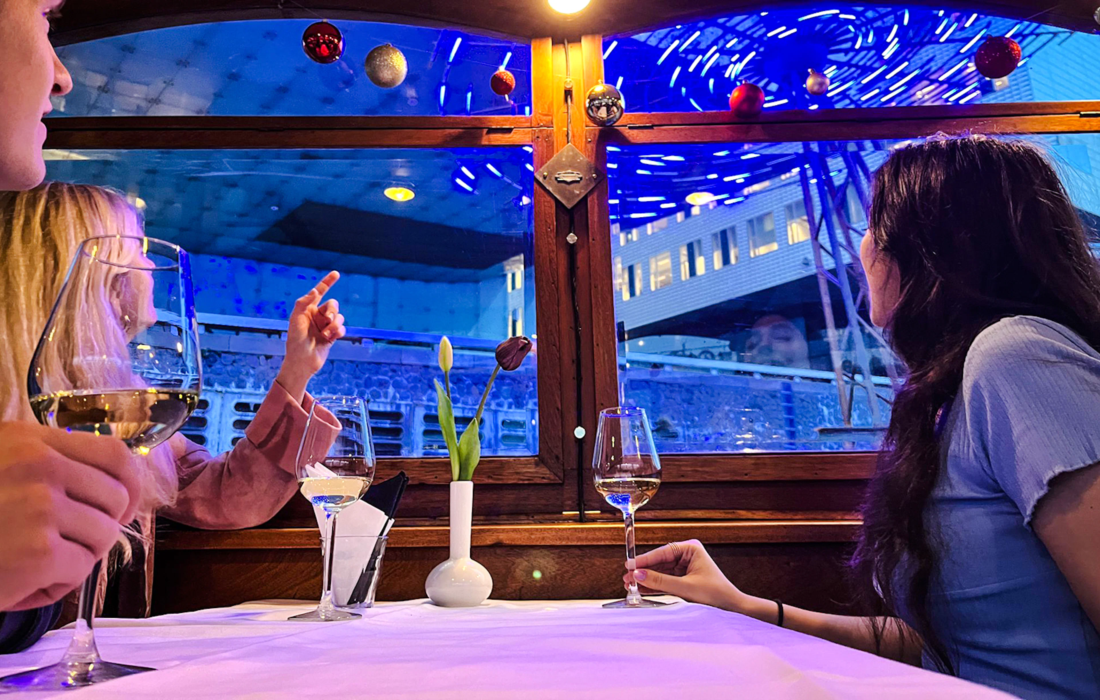Guests enjoying wine on Amsterdam Light Festival cruise with cityscape view.