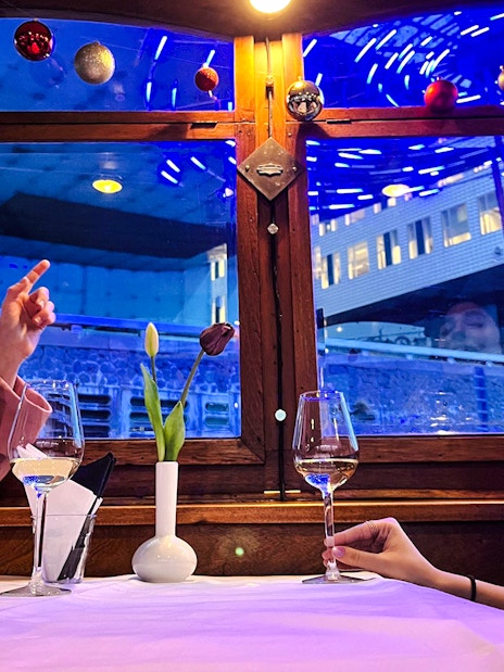 Guests enjoying wine on Amsterdam Light Festival cruise with cityscape view.